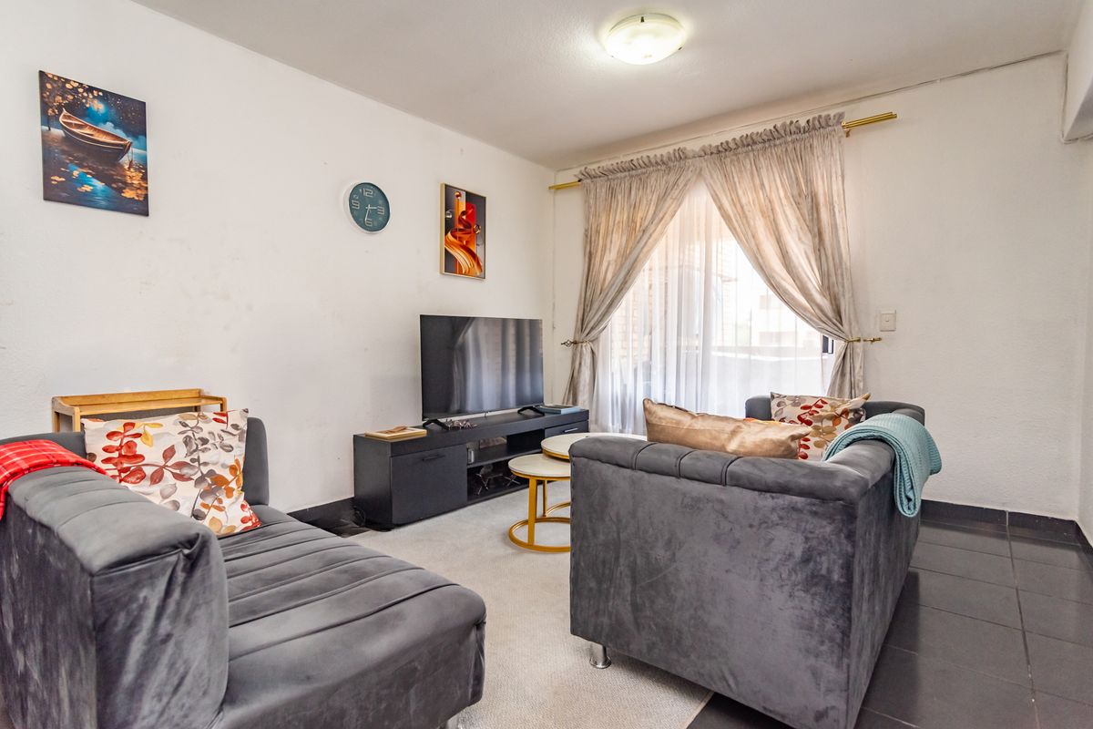 A cozy living room featuring tiled flooring, a central ceiling light, and large windows dressed with curtains, providing access to the exterior.
