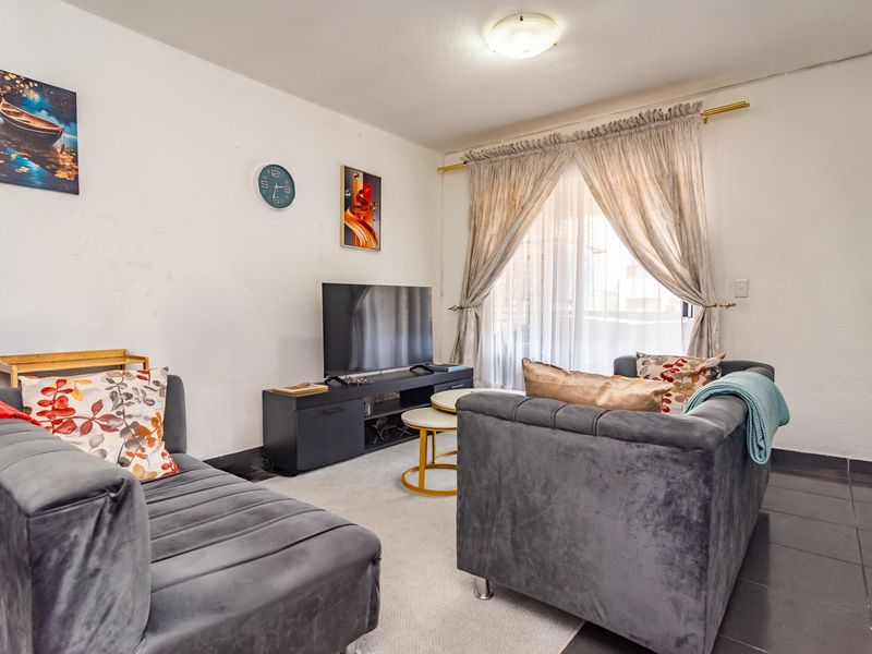A cozy living room featuring tiled flooring, a central ceiling light, and large windows dressed with curtains, providing access to the exterior.