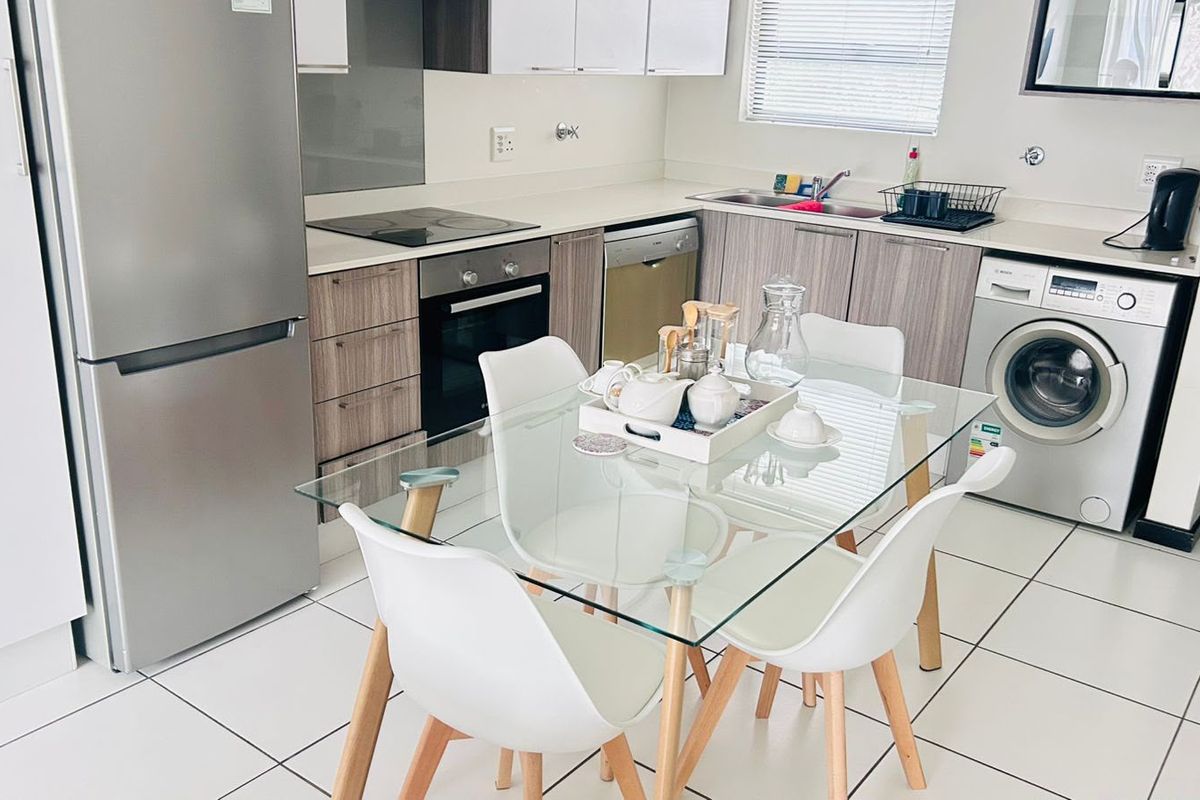 Modern open-plan kitchen featuring sleek cabinetry, integrated appliances, and tiled flooring, seamlessly flowing into the dining area.