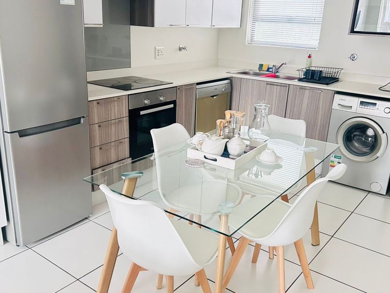 Modern open-plan kitchen featuring sleek cabinetry, integrated appliances, and tiled flooring, seamlessly flowing into the dining area.