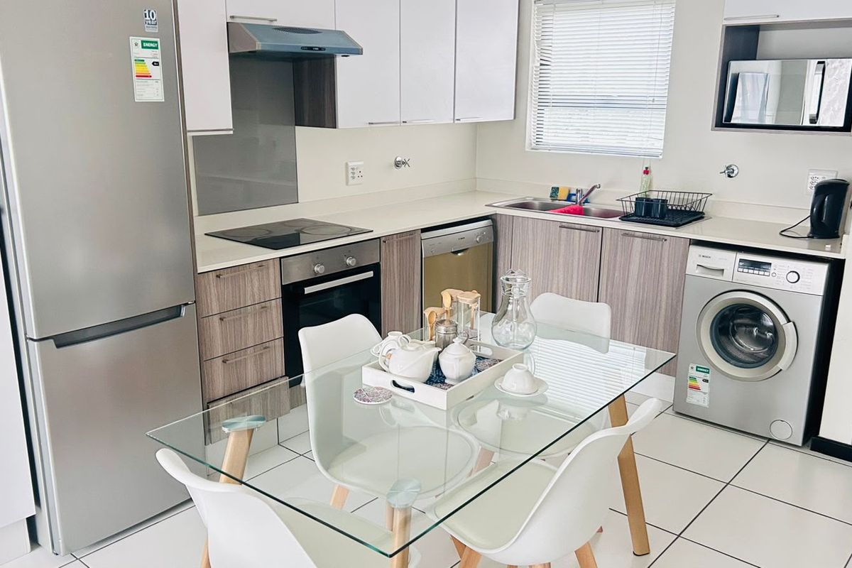 Modern open-plan kitchen featuring sleek cabinetry, integrated appliances, and tiled flooring, seamlessly flowing into the dining area.