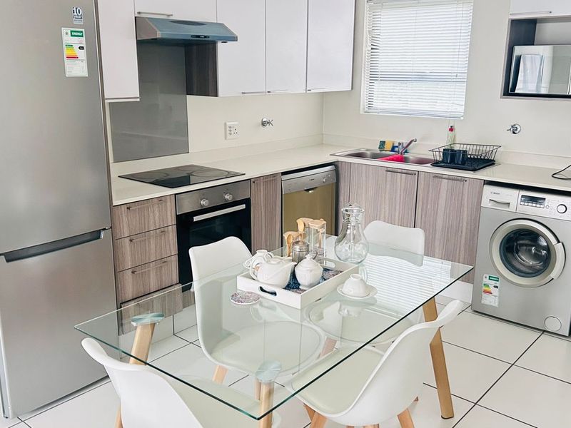 Modern open-plan kitchen featuring sleek cabinetry, integrated appliances, and tiled flooring, seamlessly flowing into the dining area.