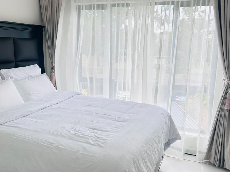 A bright bedroom featuring large sliding glass doors with floor-to-ceiling curtains and neutral tiled flooring.