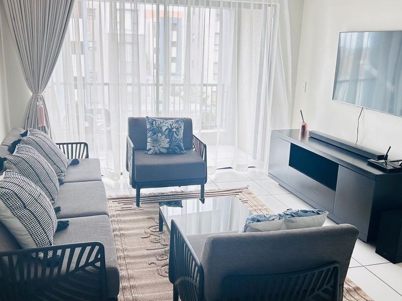 A bright and modern living room featuring tiled flooring and large sliding glass doors that provide access to the balcony.