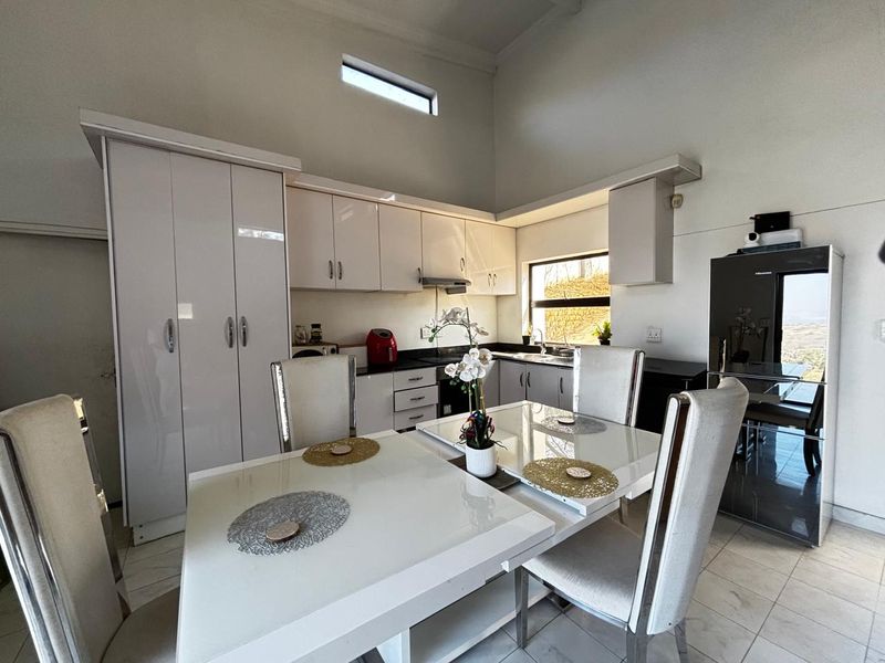 Modern open-plan kitchen and dining area featuring high-gloss cabinetry, built-in appliances, tiled flooring, and a bright, airy atmosphere with high ceilings.