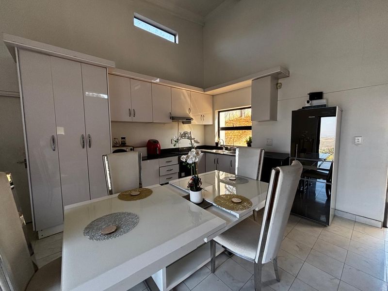 Modern open-plan kitchen and dining area featuring high ceilings, sleek white cabinetry, tiled flooring, and a bright, airy atmosphere.