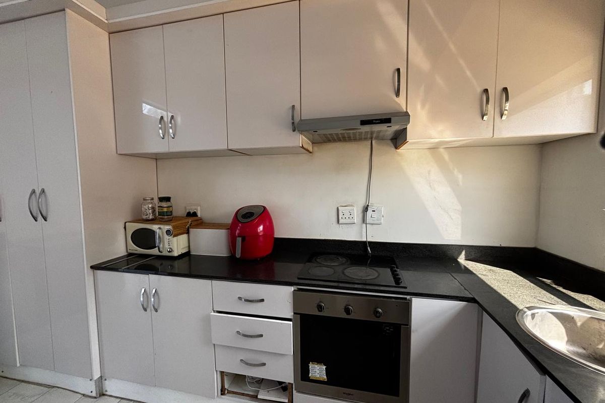 A compact kitchen featuring white cabinetry, black countertops, and integrated appliances, currently requiring minor repairs to the cabinetry.
