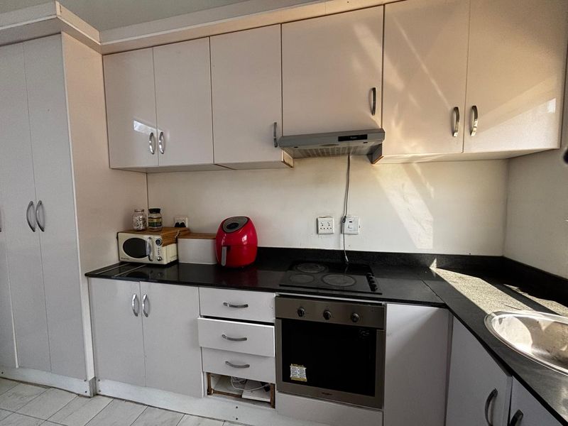 A compact kitchen featuring white cabinetry, black countertops, and integrated appliances, currently requiring minor repairs to the cabinetry.