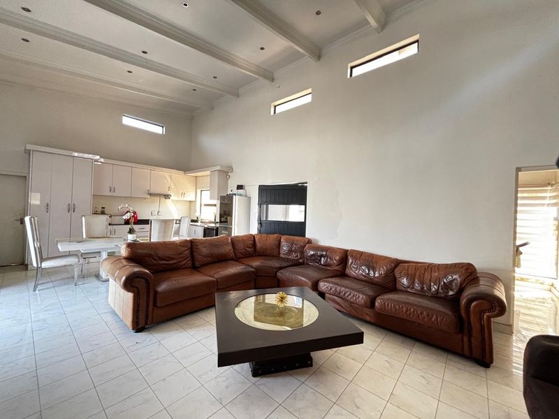 Spacious open-plan living and kitchen area featuring high ceilings with exposed beams, tiled flooring, and modern kitchen cabinetry.