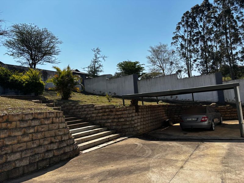 Front exterior view featuring a concrete driveway, a covered carport, tiered retaining walls, and concrete stairs leading up to the property.