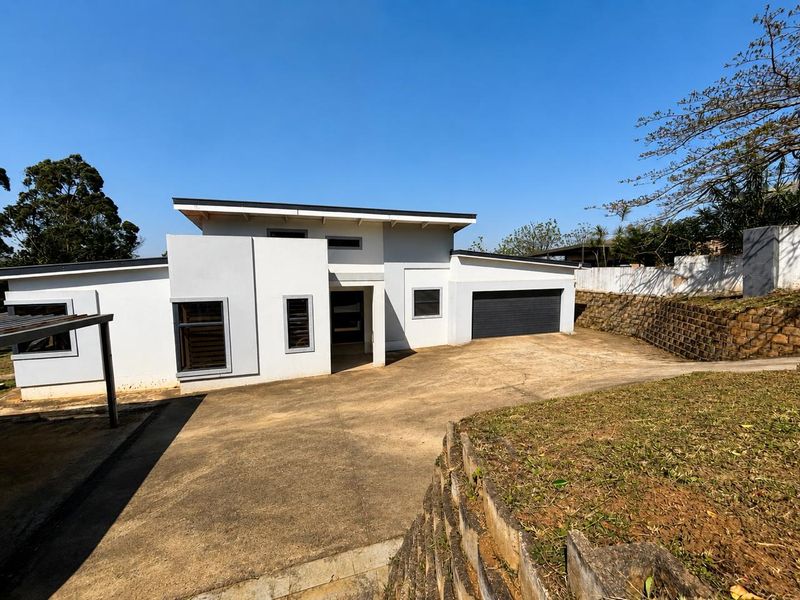 Front exterior view of a modern single-story house featuring a concrete driveway, integrated garage, and retaining wall landscaping.