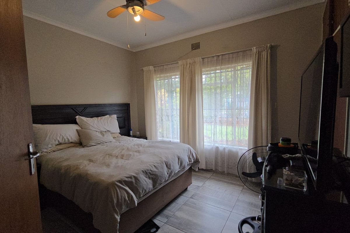 A functional bedroom featuring tiled flooring, a ceiling fan, and large windows that provide natural light.
