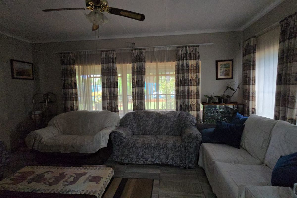 A spacious living room featuring tiled flooring and a ceiling fan, with large windows providing natural light and access to the exterior.