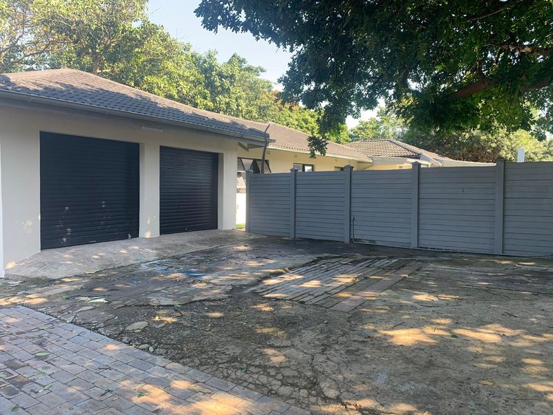Front exterior view featuring a double garage with roller shutter doors and a paved driveway area requiring maintenance.