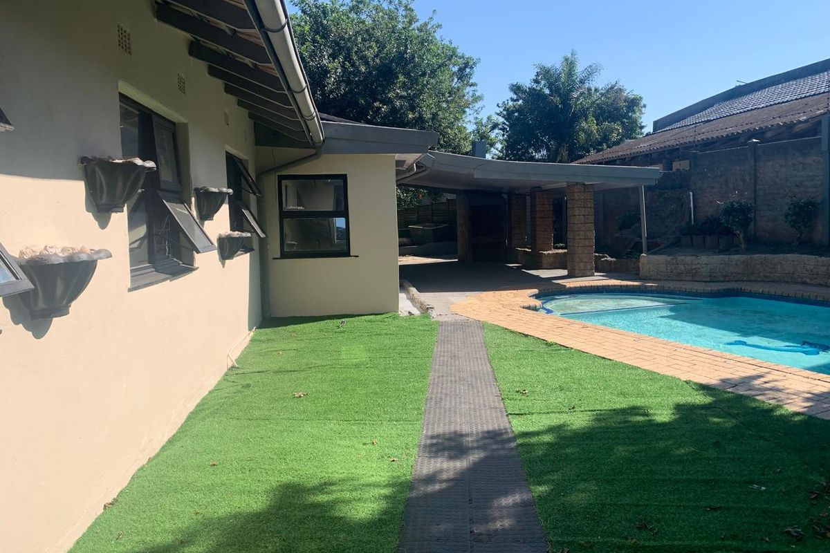 Rear exterior view featuring a swimming pool, covered patio area, brick paving, and artificial lawn, providing a functional outdoor entertainment space.