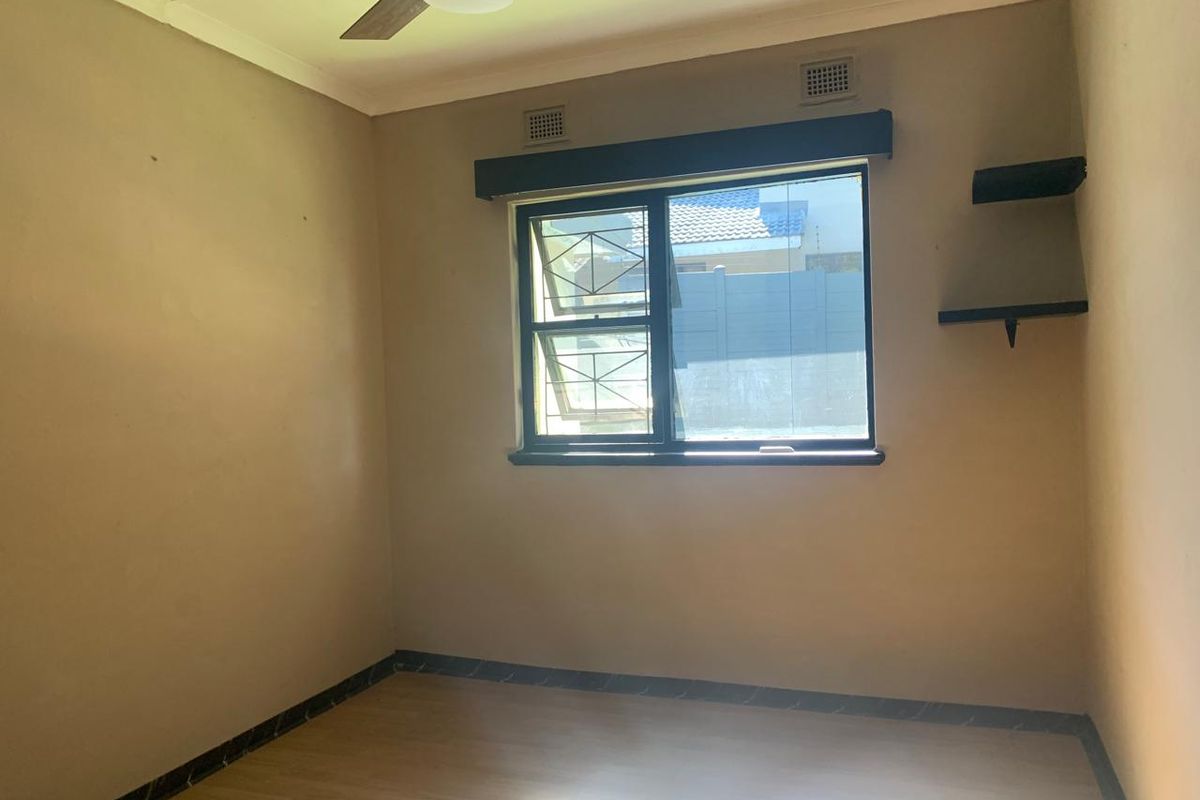 An empty bedroom featuring laminate flooring, a ceiling fan, and a window with security bars, providing a neutral canvas for personalization.