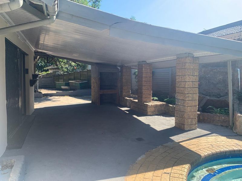Covered outdoor patio area featuring a built-in braai, stone-clad support pillars, and direct access to the adjacent swimming pool.