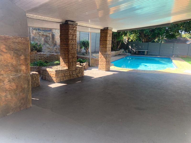 Spacious covered patio area featuring stone-clad pillars, overlooking a private swimming pool and landscaped garden.