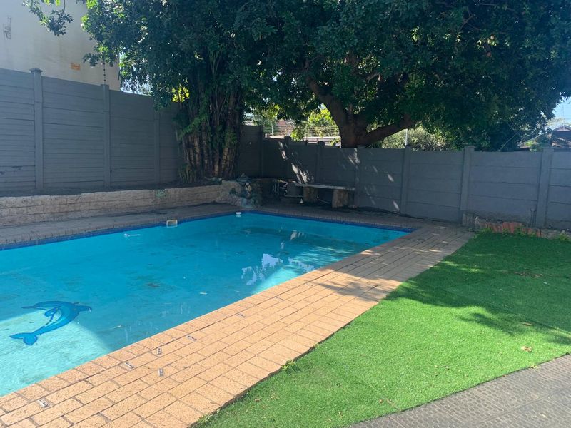Outdoor pool area featuring a swimming pool, paved surround, artificial lawn, and perimeter boundary wall with electric fencing.