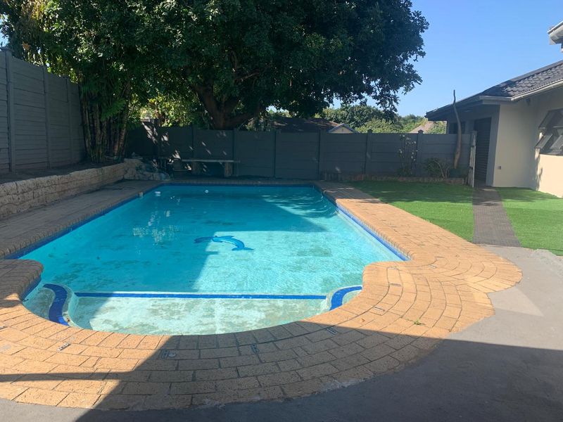 Outdoor pool area featuring a swimming pool with brick coping, artificial lawn, and perimeter fencing.