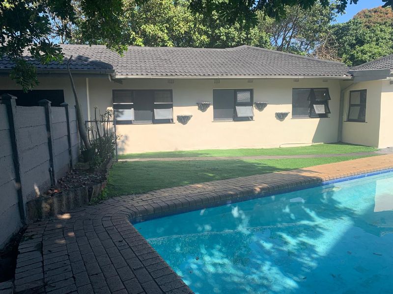 A rear exterior view featuring a swimming pool with brick paving, artificial lawn, and a single-story building with a tiled roof.
