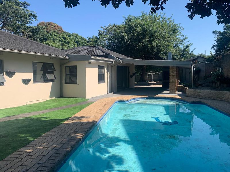 Outdoor pool area featuring a swimming pool with brick coping, an adjacent covered patio, and artificial lawn landscaping.