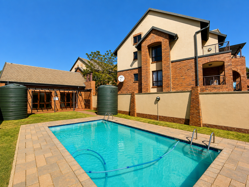 A well-maintained outdoor pool area featuring brick paving, large water storage tanks, and a view of the multi-story apartment building facade.