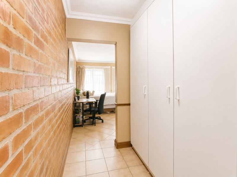 A hallway featuring an exposed brick wall, tiled flooring, and ample built-in cupboard storage, leading into an adjacent bedroom space.