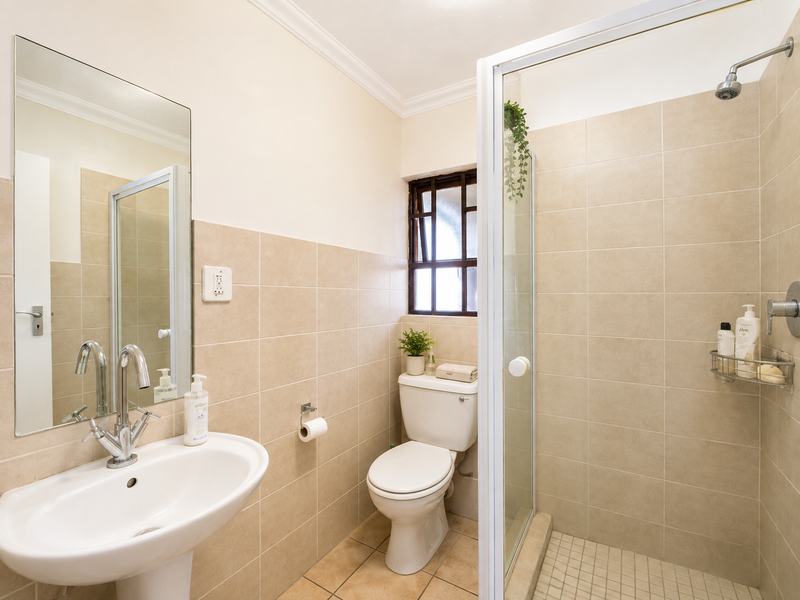 A clean and functional bathroom featuring a pedestal sink, a glass-enclosed shower, and neutral wall tiling.