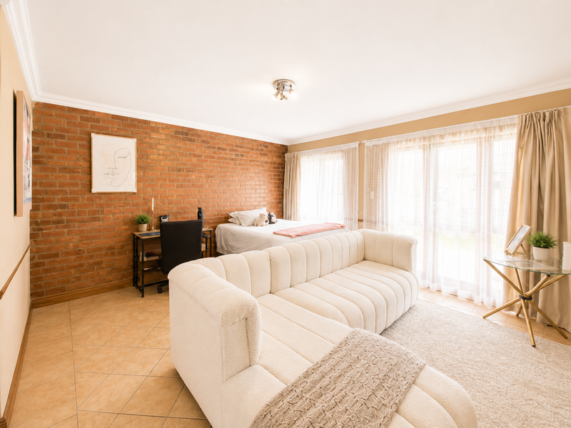 Spacious bedroom featuring an exposed brick feature wall, tiled flooring, and large sliding glass doors providing ample natural light.