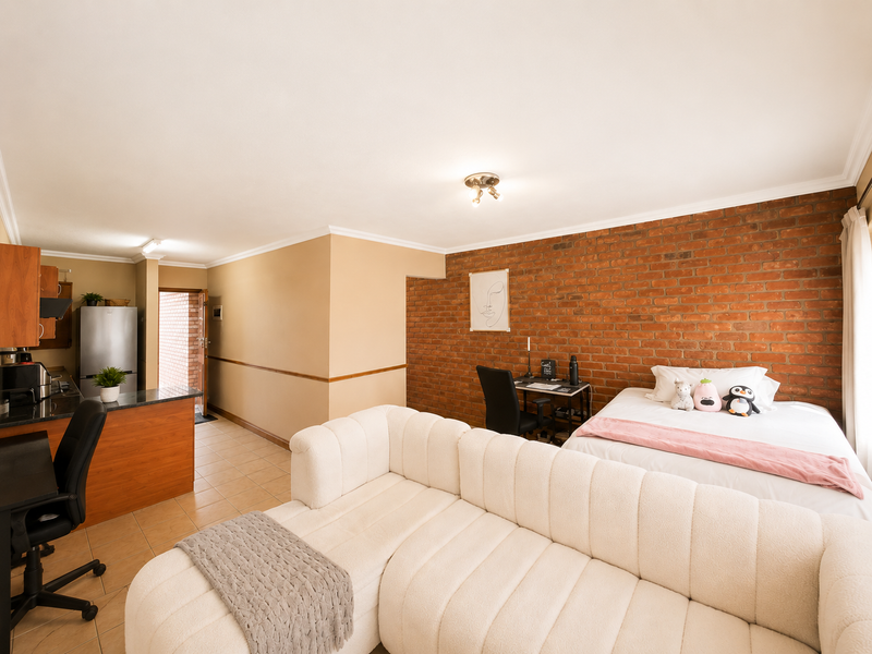 Open-plan studio apartment featuring an exposed brick feature wall, tiled flooring, and a functional kitchen area with granite countertops.