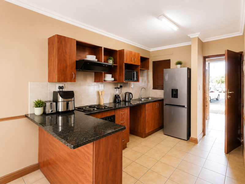 A functional kitchen featuring wooden cabinetry, granite countertops, a built-in hob, and tiled flooring, with direct access to an exterior entrance.