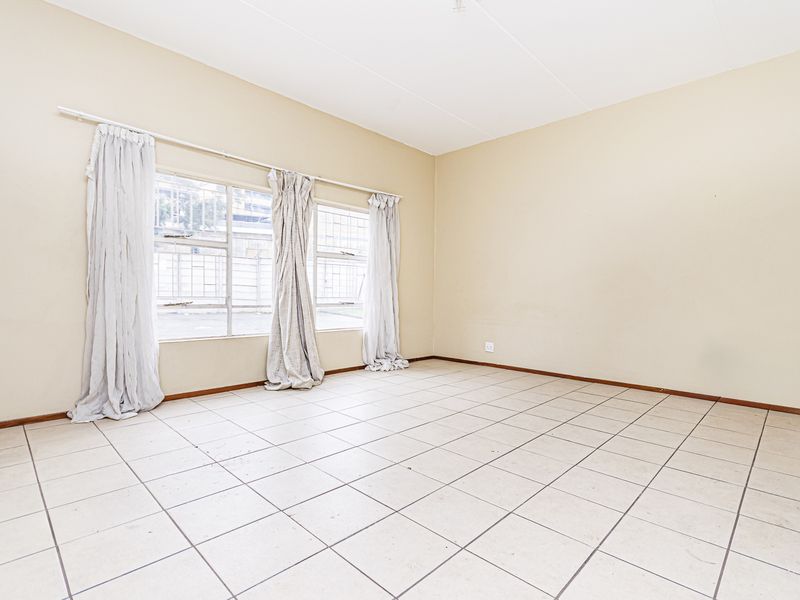 A spacious, empty living area featuring neutral tiled flooring and large windows with security bars, offering a blank canvas for personalization.