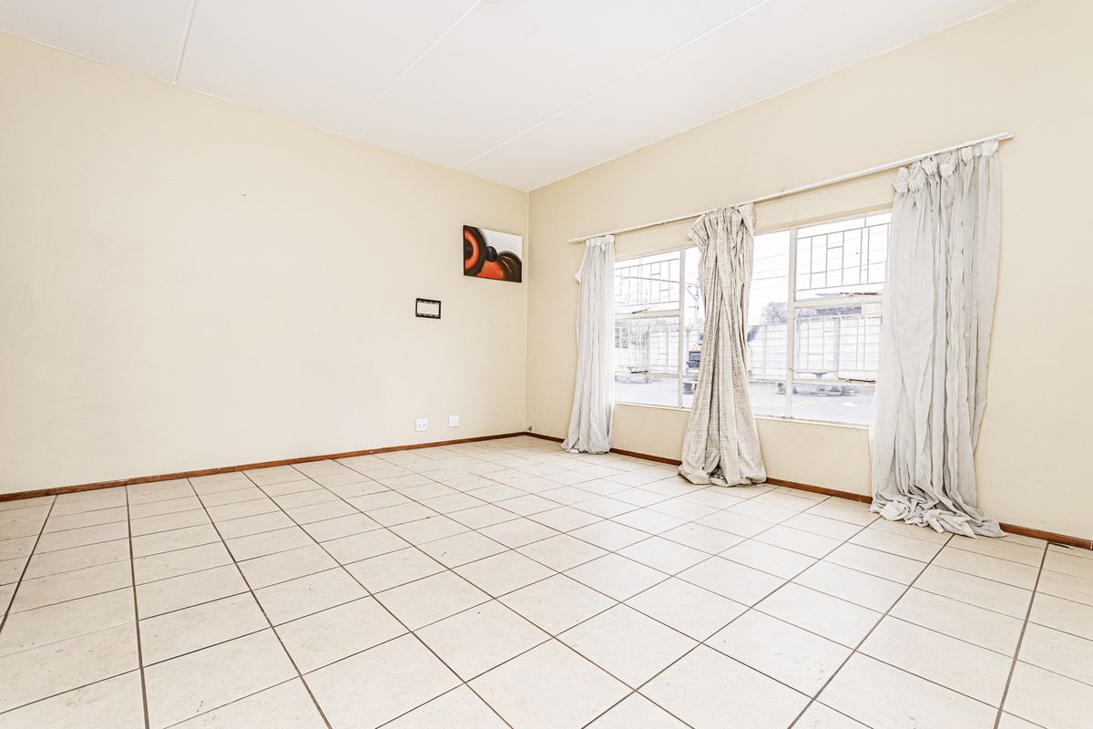 An empty living room featuring tiled flooring and large windows with security bars, offering a blank canvas for potential interior design updates.