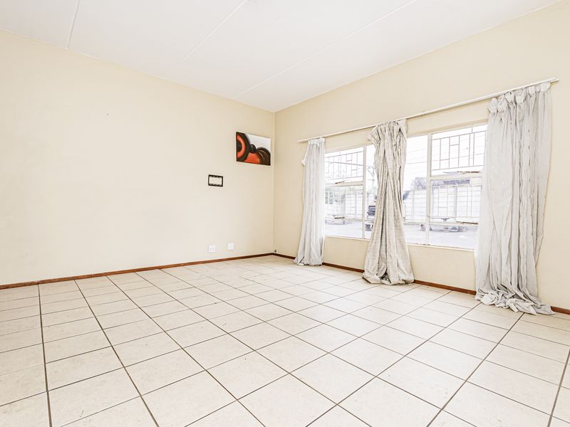 An empty living room featuring tiled flooring and large windows with security bars, offering a blank canvas for potential interior design updates.
