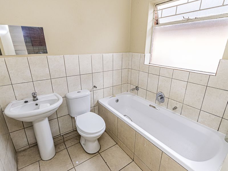 A functional bathroom featuring a pedestal basin, toilet, and bathtub with neutral wall and floor tiling.