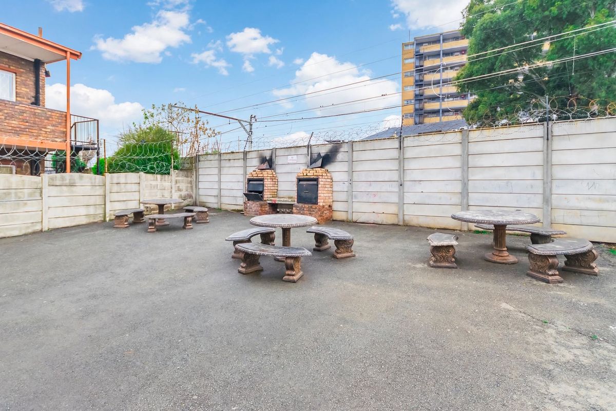 Communal outdoor courtyard area featuring built-in brick braai facilities and paved flooring, enclosed by precast concrete walls with security fencing.