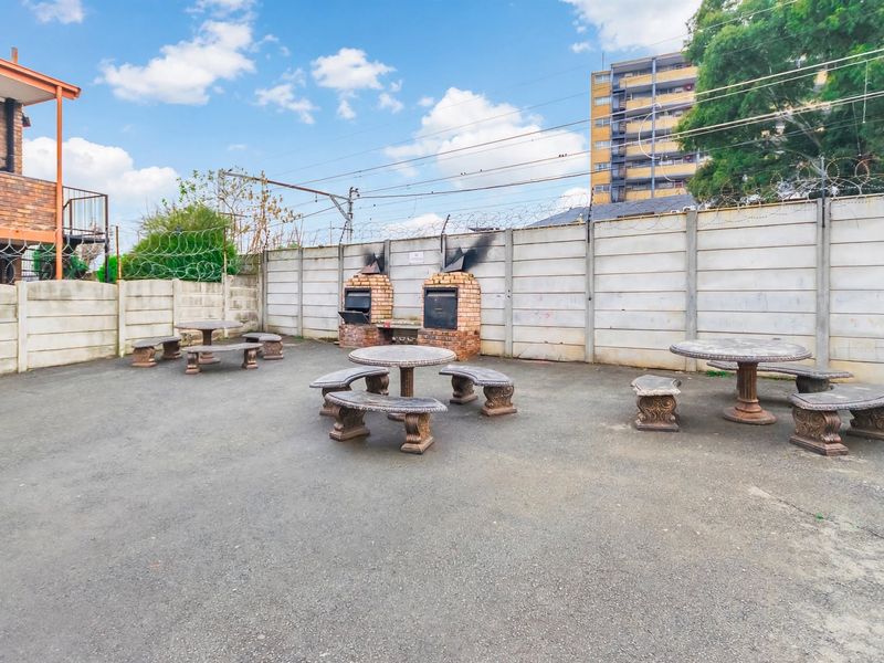 Communal outdoor courtyard area featuring built-in brick braai facilities and paved flooring, enclosed by precast concrete walls with security fencing.