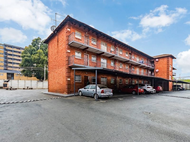 Exterior view of a multi-story face brick apartment building featuring covered parking bays and private balconies for each unit.
