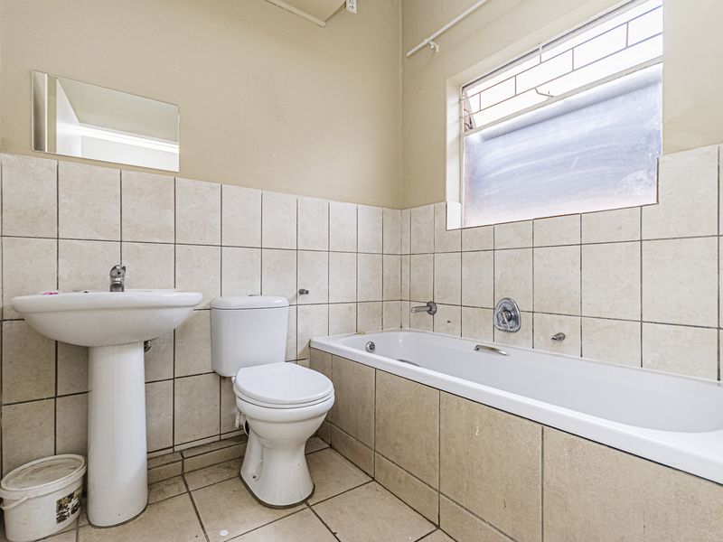 A dated bathroom featuring a pedestal basin, standard toilet, and bathtub with tiled walls and flooring, offering potential for modernization.