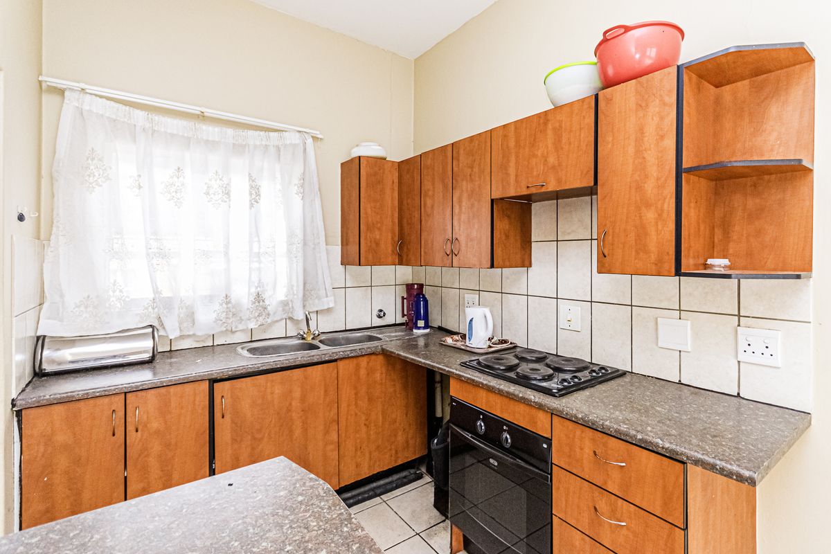 A functional kitchen featuring wood-look cabinetry, a built-in oven with electric hob, double sink, and tiled splashbacks, offering a practical layout for daily use.