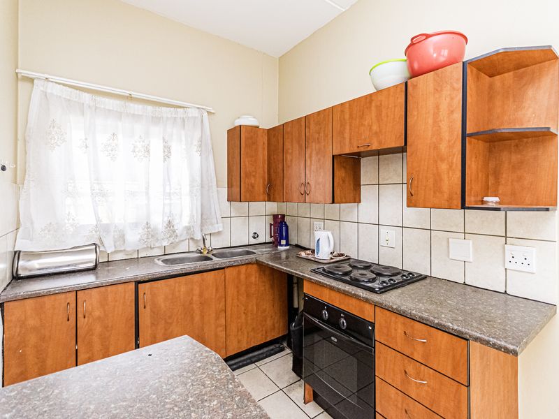 A functional kitchen featuring wood-look cabinetry, a built-in oven with electric hob, double sink, and tiled splashbacks, offering a practical layout for daily use.