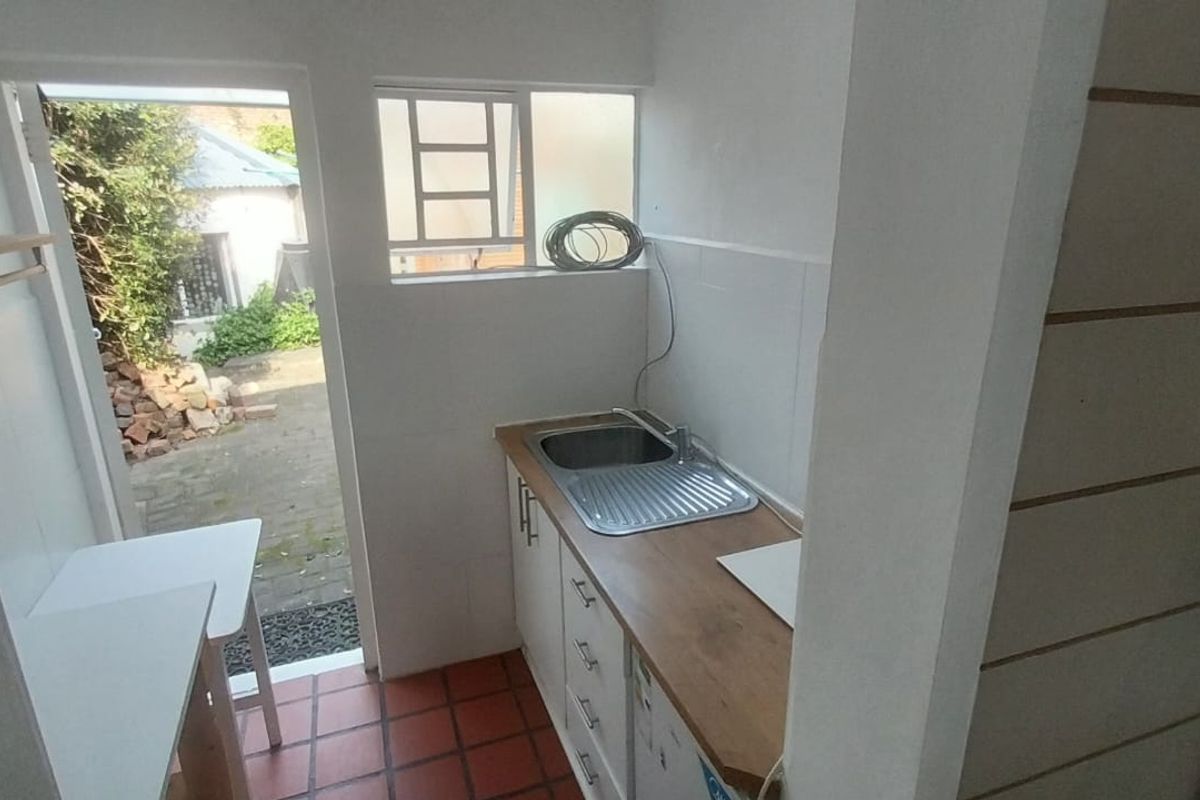 A functional scullery or utility area featuring built-in cabinetry, a stainless steel sink, timber countertop, and direct access to the rear exterior.