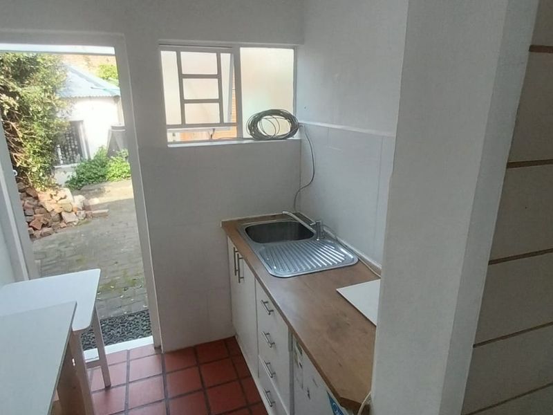 A functional scullery or utility area featuring built-in cabinetry, a stainless steel sink, timber countertop, and direct access to the rear exterior.
