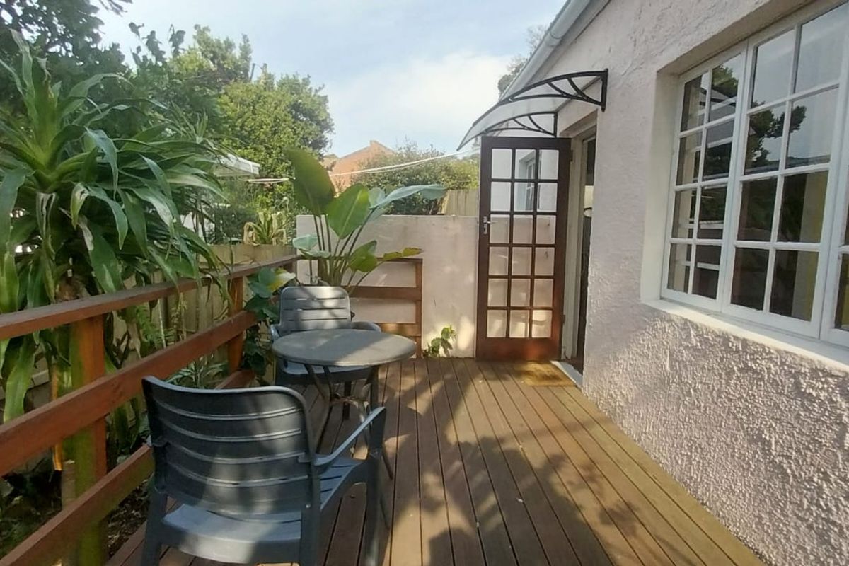 A timber-decked patio area featuring a wooden balustrade, a classic french door entrance, and a protective door canopy, providing a cozy outdoor seating space.
