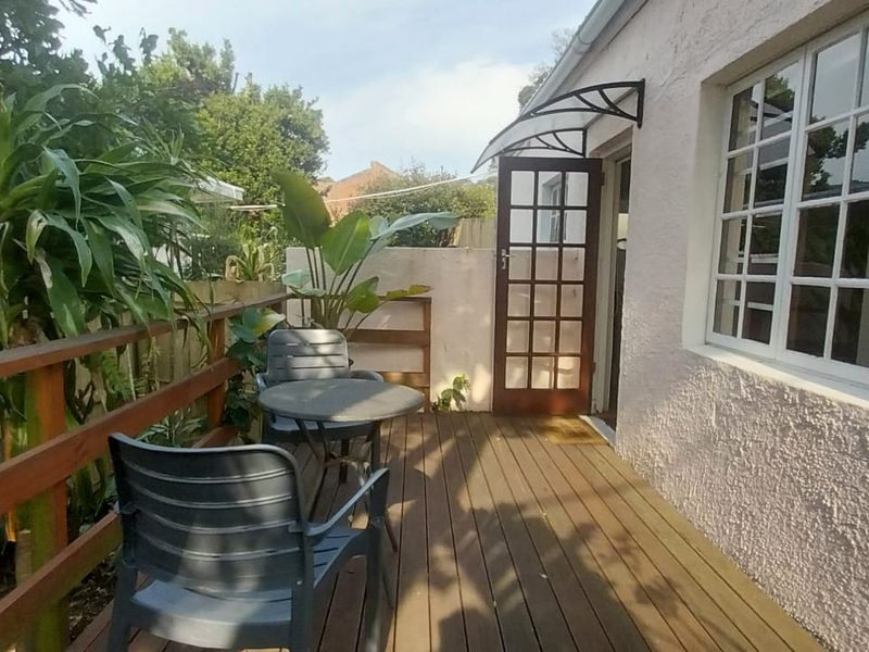 A timber-decked patio area featuring a wooden balustrade, a classic french door entrance, and a protective door canopy, providing a cozy outdoor seating space.
