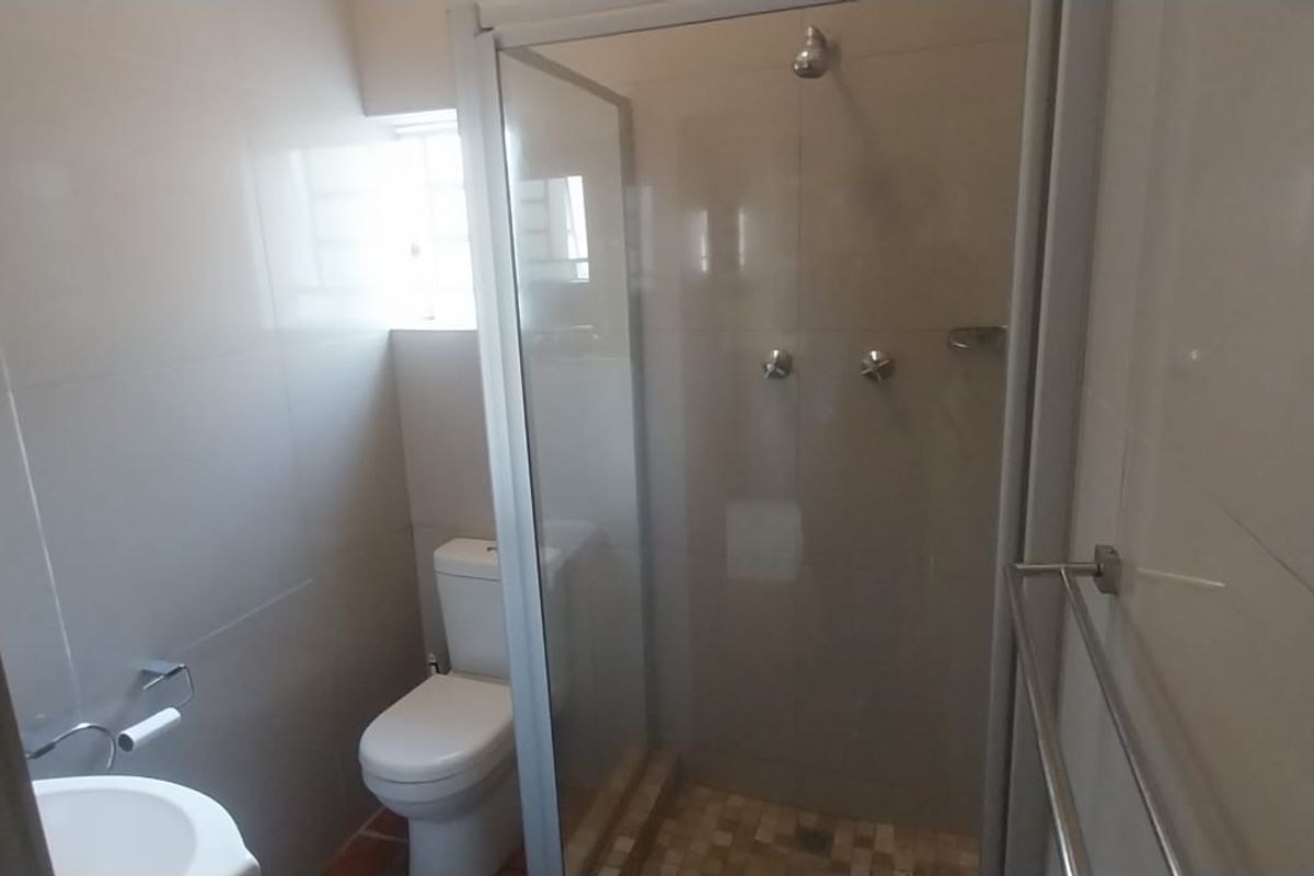 A clean, functional bathroom featuring a glass-enclosed shower, modern toilet, wash basin, and neutral wall tiling.