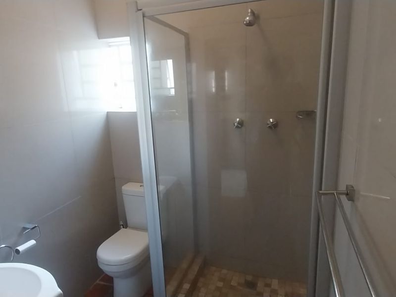 A clean, functional bathroom featuring a glass-enclosed shower, modern toilet, wash basin, and neutral wall tiling.