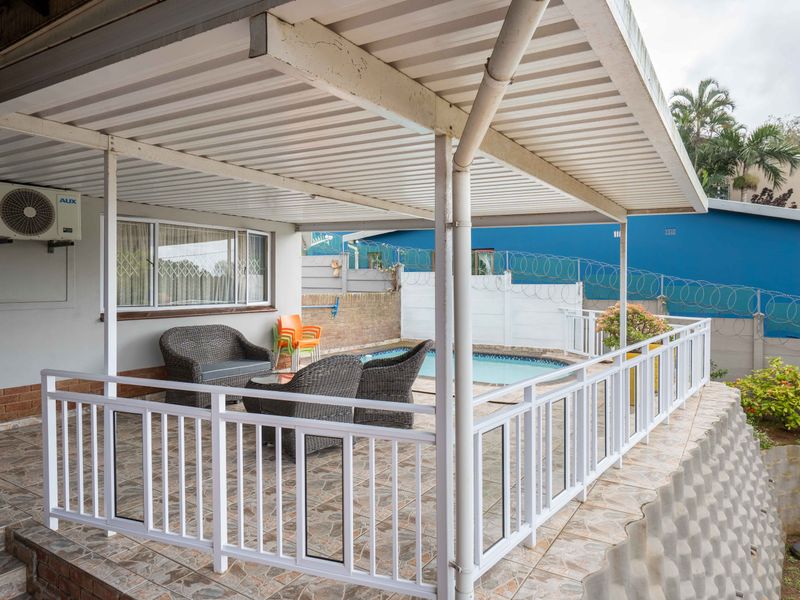 Covered outdoor patio area featuring tiled flooring, white metal railings, and direct access to the swimming pool and garden area.