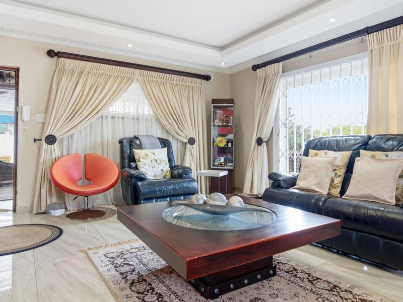 A well-maintained living room featuring tiled flooring, recessed ceiling with downlights, and large windows with security gates leading to an outdoor area.